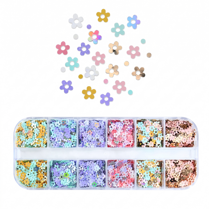 A clear plastic tray filled with small flower-shaped craft embellishments in multiple pastel and metallic colors, with additional loose flower pieces scattered above on a white background.