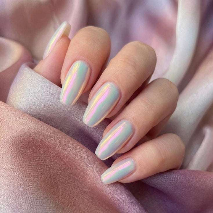 Close-up of a hand with pastel nail polish on a soft pink fabric background